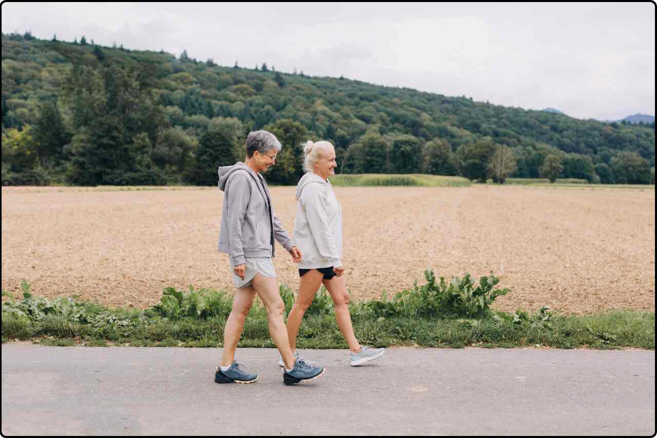 Elderly woman and man with hiking gear walking through a road beside by hill.